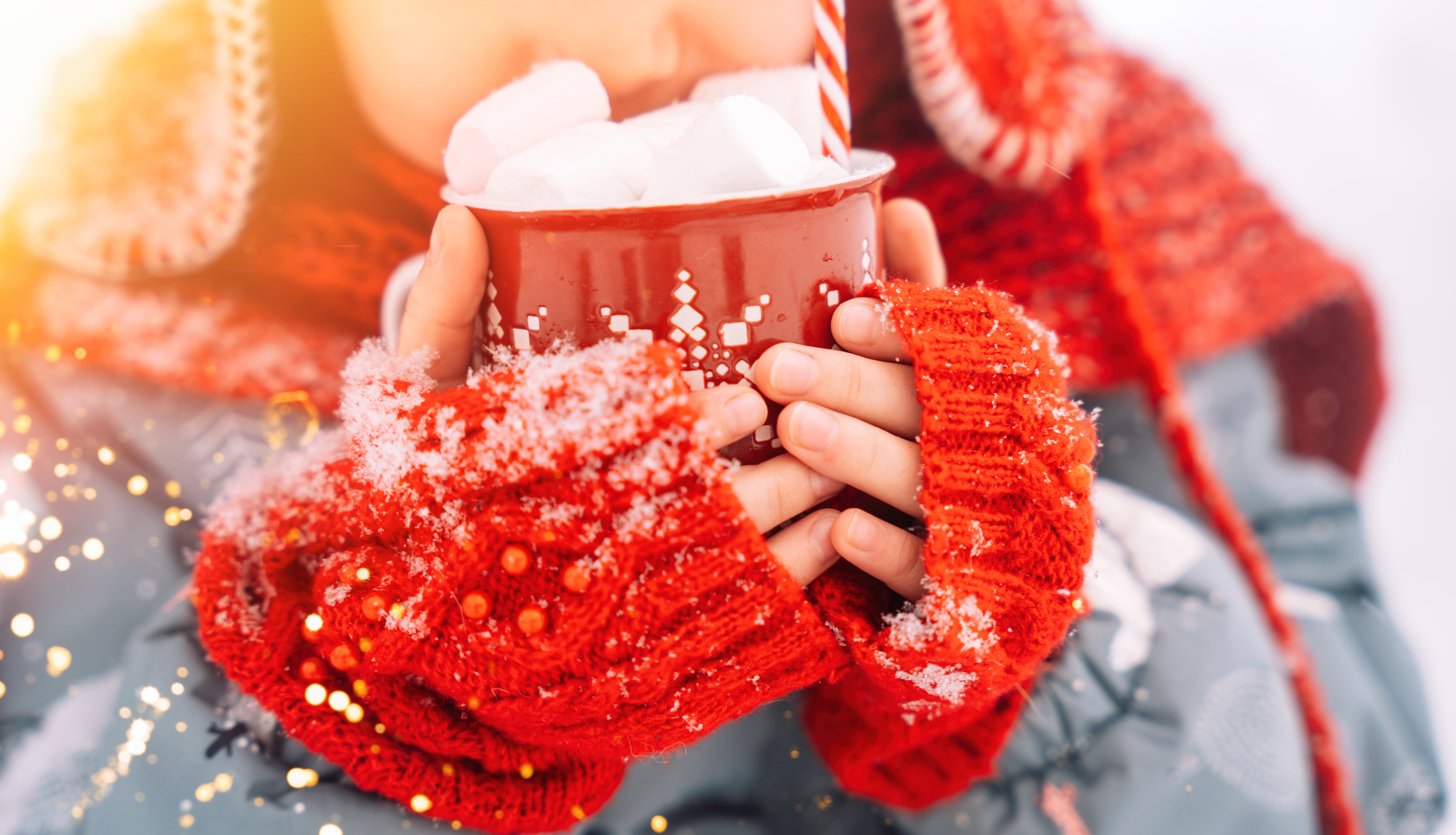 Barn som held ein kopp varm kakao med marshmallows ute i snøen.